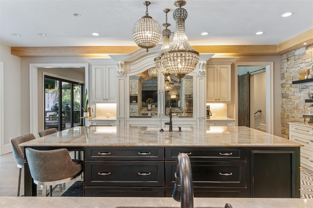 kitchen with a notable chandelier, a barn door, light stone counters, and an island with sink