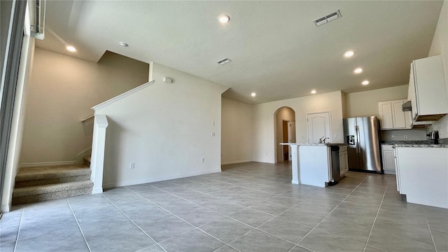 kitchen featuring light stone countertops, a kitchen island with sink, light tile patterned flooring, white cabinetry, and stainless steel fridge with ice dispenser