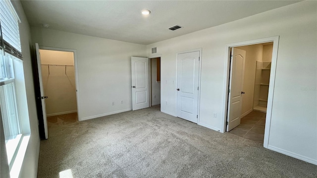 unfurnished bedroom featuring a spacious closet, light colored carpet, and connected bathroom