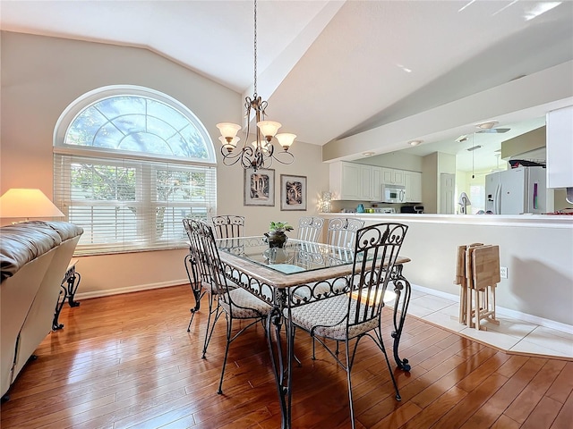 dining room featuring a notable chandelier, vaulted ceiling, and light wood-type flooring