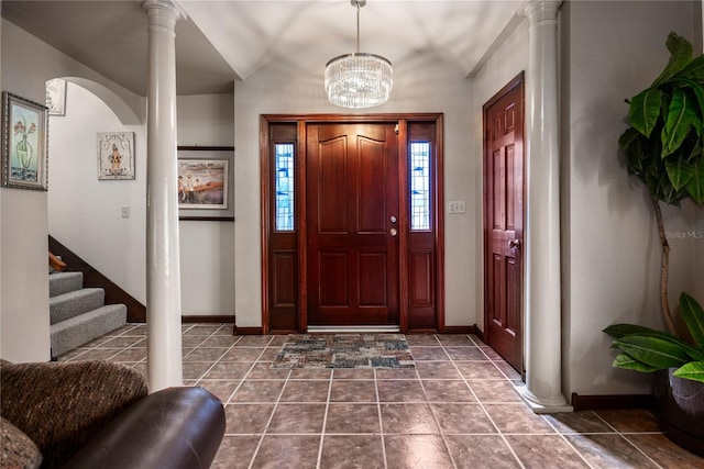 foyer entrance with an inviting chandelier, lofted ceiling, decorative columns, and dark tile patterned flooring