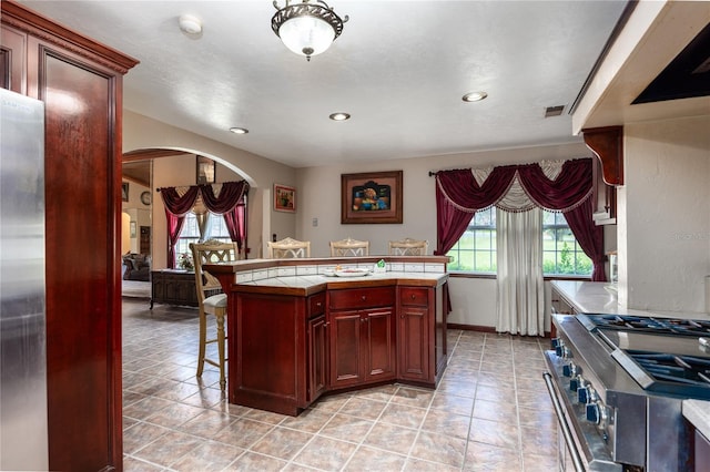 kitchen featuring tile counters, a center island, a kitchen bar, light tile patterned floors, and appliances with stainless steel finishes