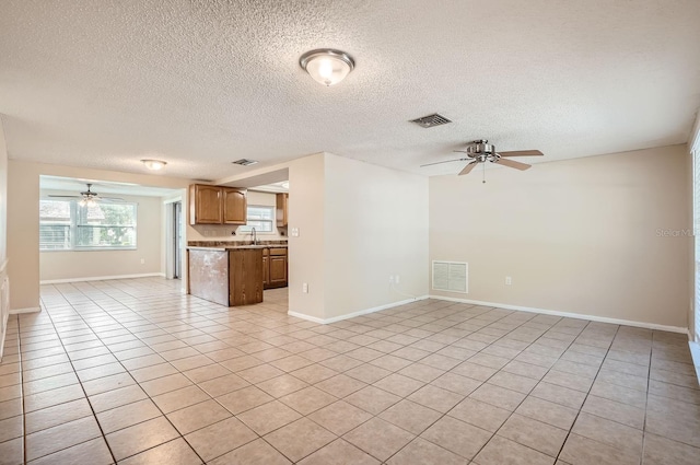 unfurnished living room featuring a textured ceiling, ceiling fan, sink, and light tile patterned floors