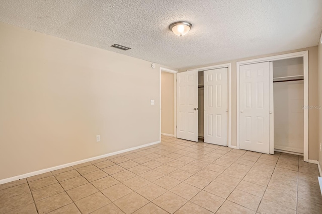 unfurnished bedroom featuring light tile patterned flooring, a textured ceiling, and two closets