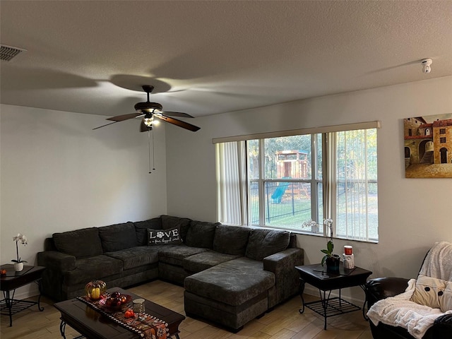 living room with ceiling fan, light wood-type flooring, and a textured ceiling