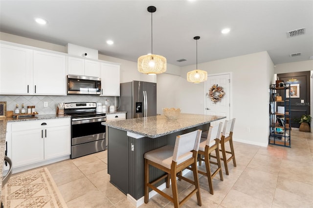 kitchen featuring light stone countertops, appliances with stainless steel finishes, a center island, pendant lighting, and white cabinets