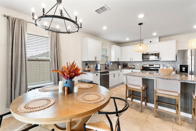 kitchen featuring white cabinets, appliances with stainless steel finishes, light stone countertops, a chandelier, and pendant lighting