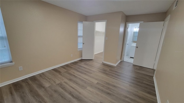 unfurnished bedroom featuring connected bathroom, a closet, a walk in closet, and light hardwood / wood-style floors