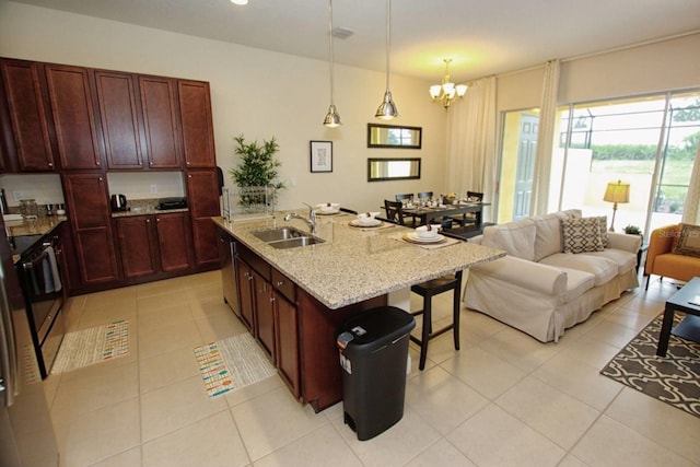 kitchen featuring sink, an island with sink, light stone counters, a breakfast bar, and a chandelier