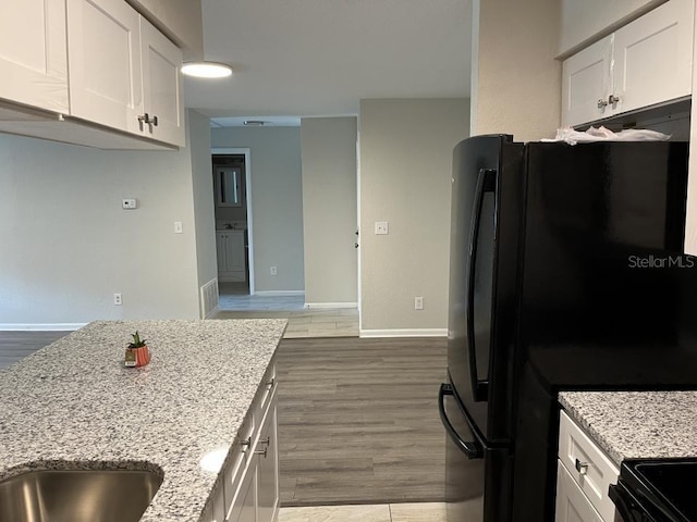 kitchen with black fridge, light hardwood / wood-style flooring, and white cabinetry