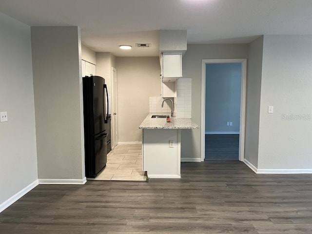 kitchen featuring dark wood-type flooring, black fridge, sink, backsplash, and white cabinets