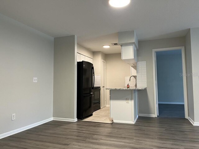 kitchen with black fridge, light stone countertops, dark hardwood / wood-style floors, and white cabinets