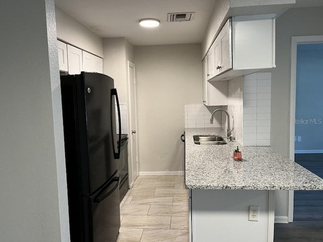 kitchen with sink, tasteful backsplash, white cabinetry, a breakfast bar, and black refrigerator