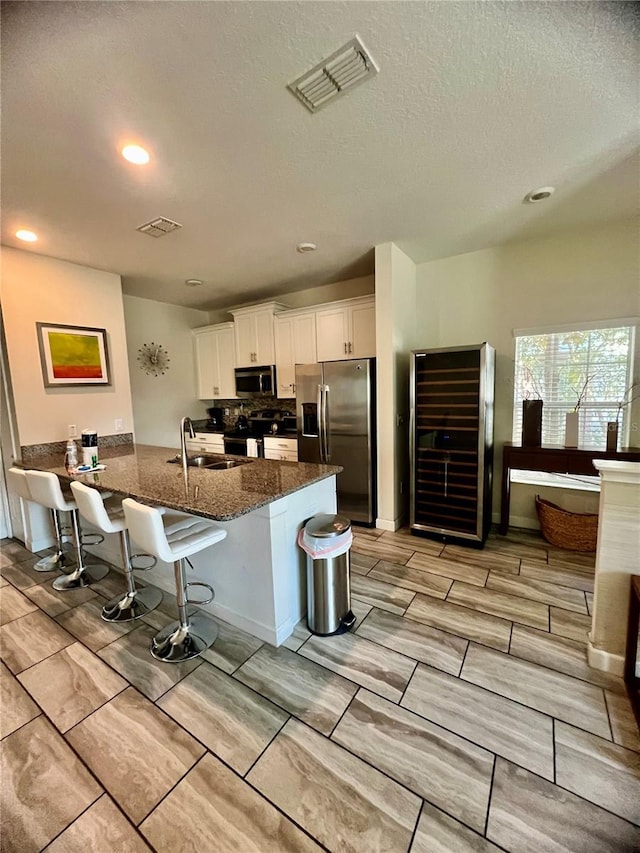 kitchen with appliances with stainless steel finishes, sink, white cabinetry, dark stone countertops, and a breakfast bar