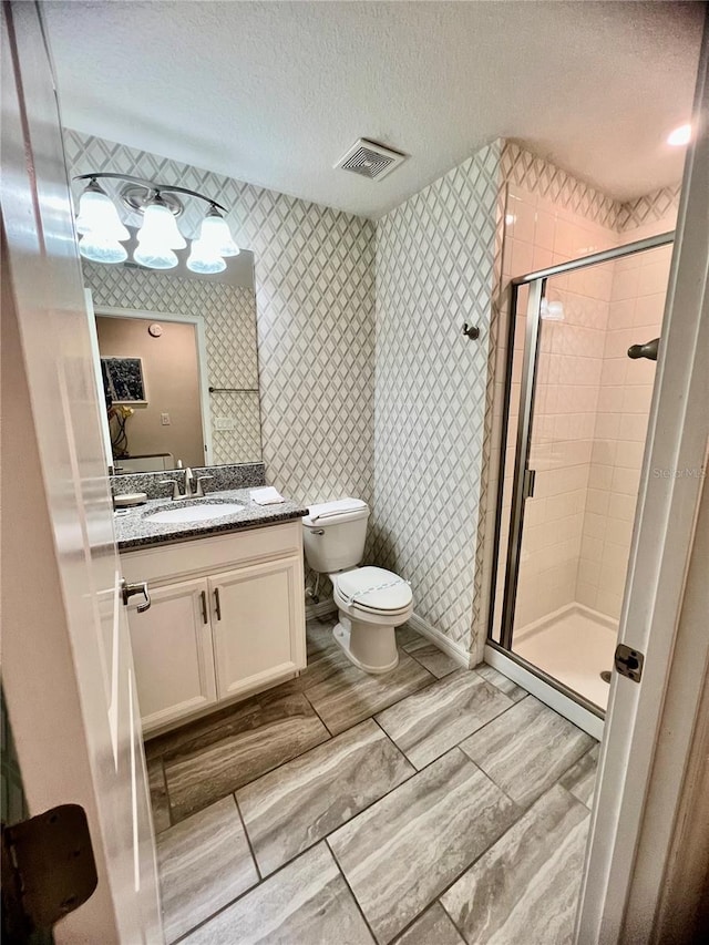 bathroom with vanity, toilet, a textured ceiling, and a shower with door