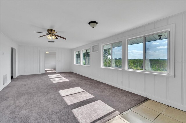 empty room featuring light carpet, visible vents, a decorative wall, and a ceiling fan