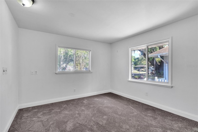 empty room with a wealth of natural light, dark carpet, and baseboards