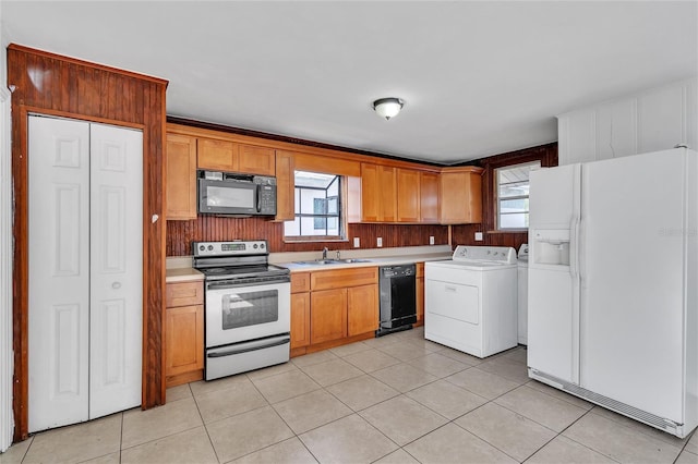 kitchen with brown cabinets, washing machine and clothes dryer, light countertops, light tile patterned flooring, and black appliances