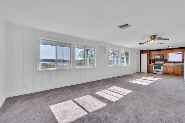 unfurnished living room with light colored carpet, visible vents, a decorative wall, a ceiling fan, and a sink