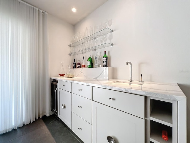 bar featuring light stone counters, dark tile patterned flooring, sink, and white cabinets