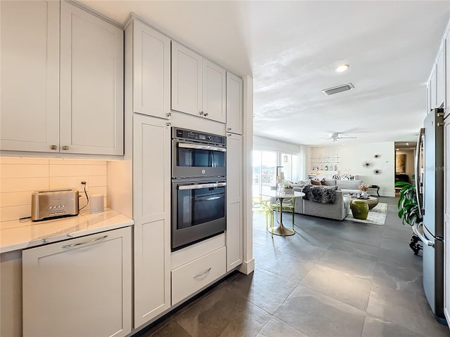 kitchen featuring light stone counters, ceiling fan, stainless steel appliances, white cabinetry, and backsplash