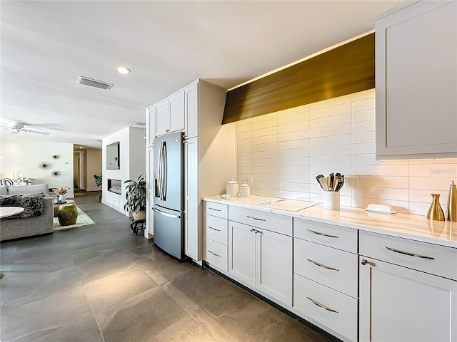 kitchen with backsplash, light stone counters, white cabinets, and stainless steel refrigerator with ice dispenser