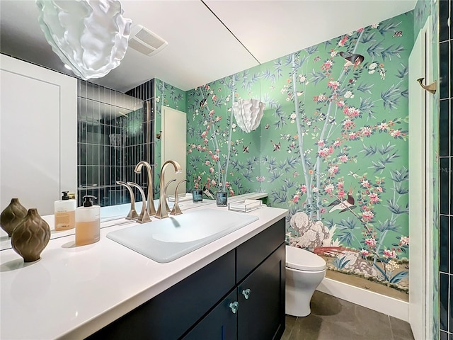 bathroom with tile patterned floors, vanity, tiled shower, and toilet