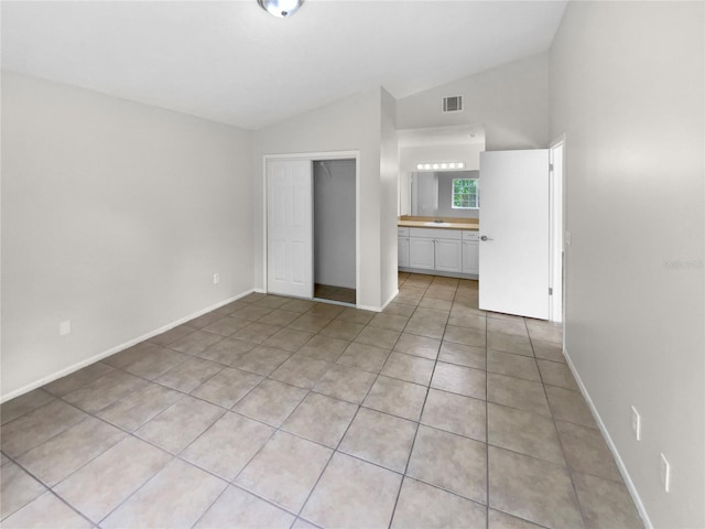 unfurnished bedroom featuring a closet, vaulted ceiling, sink, ensuite bath, and light tile patterned floors