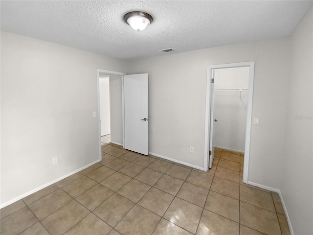 unfurnished bedroom with a spacious closet, a closet, light tile patterned floors, and a textured ceiling