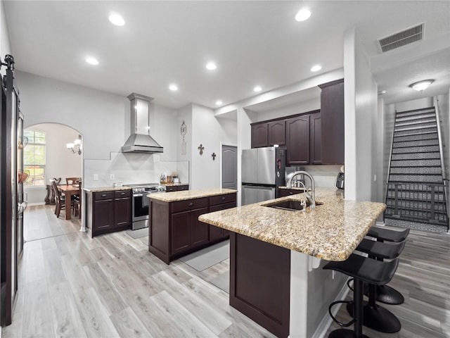 kitchen featuring sink, kitchen peninsula, stainless steel appliances, wall chimney exhaust hood, and a breakfast bar