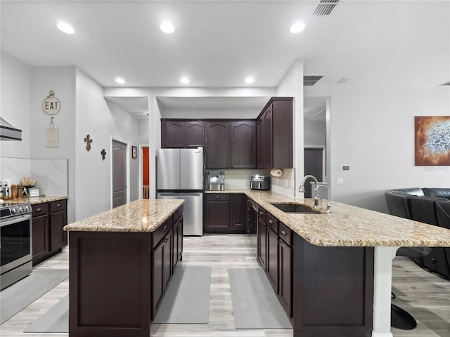 kitchen with dark brown cabinets, a kitchen island, light wood-type flooring, sink, and stainless steel appliances