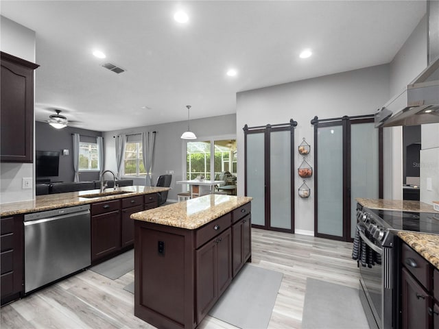 kitchen with appliances with stainless steel finishes, a barn door, sink, light hardwood / wood-style floors, and a center island