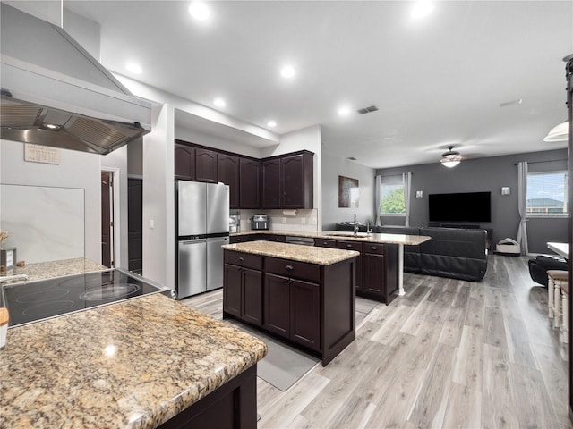 kitchen with island range hood, stainless steel fridge, kitchen peninsula, and a healthy amount of sunlight