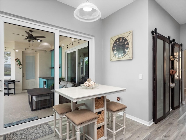 dining room with light hardwood / wood-style flooring, a barn door, and ceiling fan