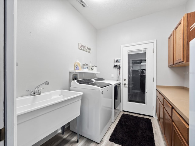 washroom featuring sink, washing machine and clothes dryer, cabinets, a textured ceiling, and light hardwood / wood-style floors