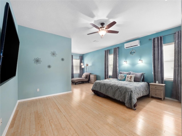 bedroom featuring multiple windows, an AC wall unit, light wood-type flooring, and ceiling fan