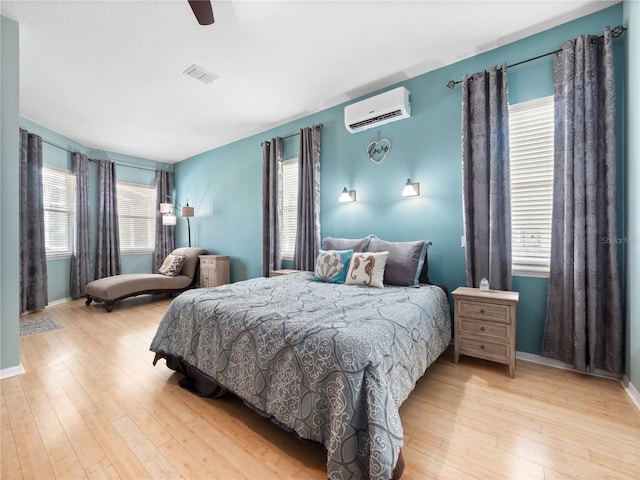 bedroom with a wall mounted AC, light wood-type flooring, and ceiling fan