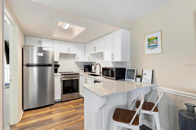 kitchen with light hardwood / wood-style floors, sink, stainless steel appliances, kitchen peninsula, and white cabinetry