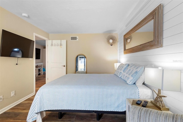bedroom with wooden walls, wood finished floors, visible vents, and baseboards