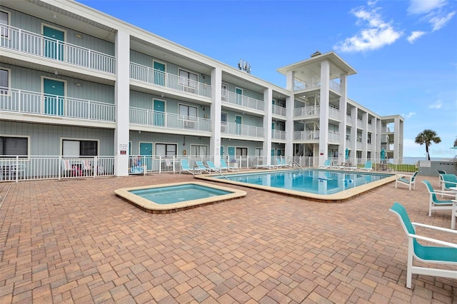 community pool with fence, a patio, and a hot tub