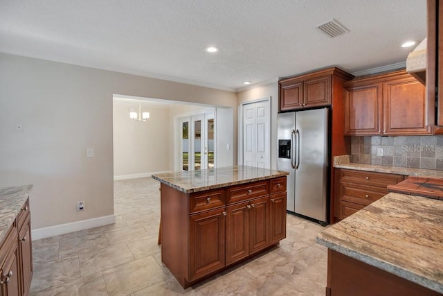 kitchen featuring a kitchen island, backsplash, ornamental molding, stainless steel fridge, and light stone counters