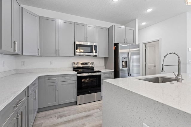 kitchen featuring light stone countertops, appliances with stainless steel finishes, light hardwood / wood-style flooring, and sink