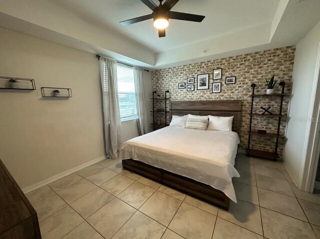 tiled bedroom featuring a tray ceiling, brick wall, and ceiling fan