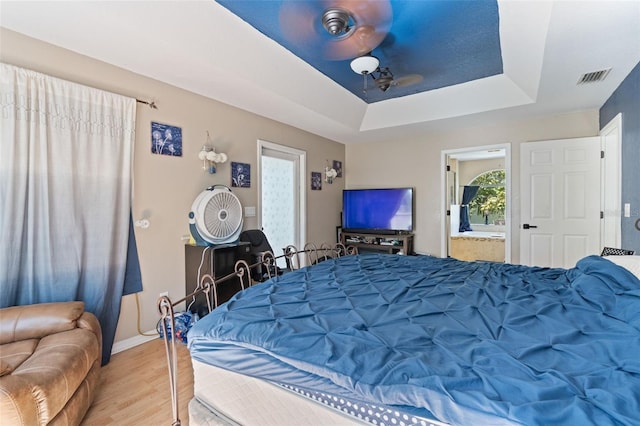 bedroom with connected bathroom, light wood-type flooring, and a raised ceiling