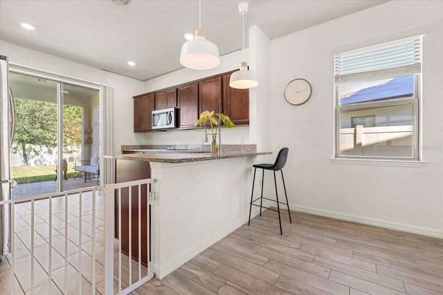 kitchen with light hardwood / wood-style flooring, hanging light fixtures, dark stone counters, and kitchen peninsula