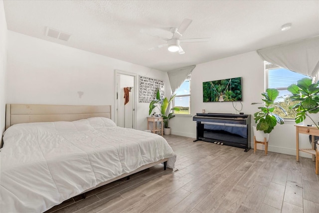 bedroom with a textured ceiling, multiple windows, light wood-type flooring, and ceiling fan