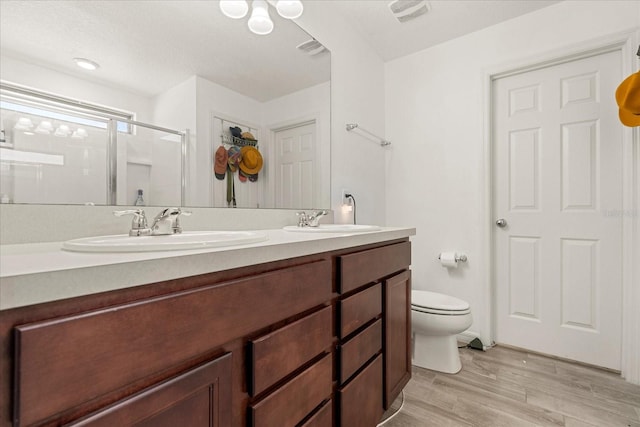 bathroom featuring vanity, hardwood / wood-style floors, a shower with shower door, and toilet