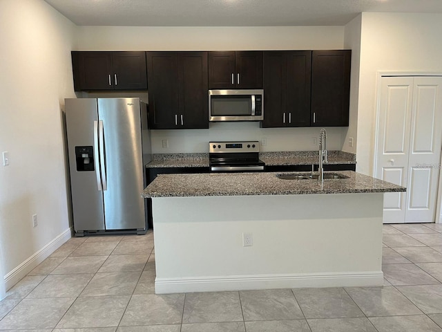 kitchen with light stone countertops, sink, appliances with stainless steel finishes, and a kitchen island with sink