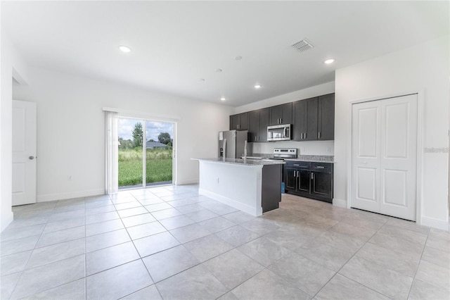 kitchen with appliances with stainless steel finishes, light stone countertops, light tile patterned flooring, and an island with sink