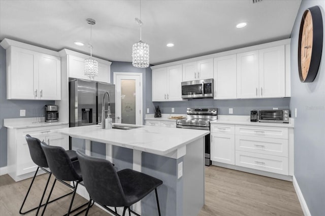 kitchen with appliances with stainless steel finishes, pendant lighting, light wood-type flooring, and white cabinets